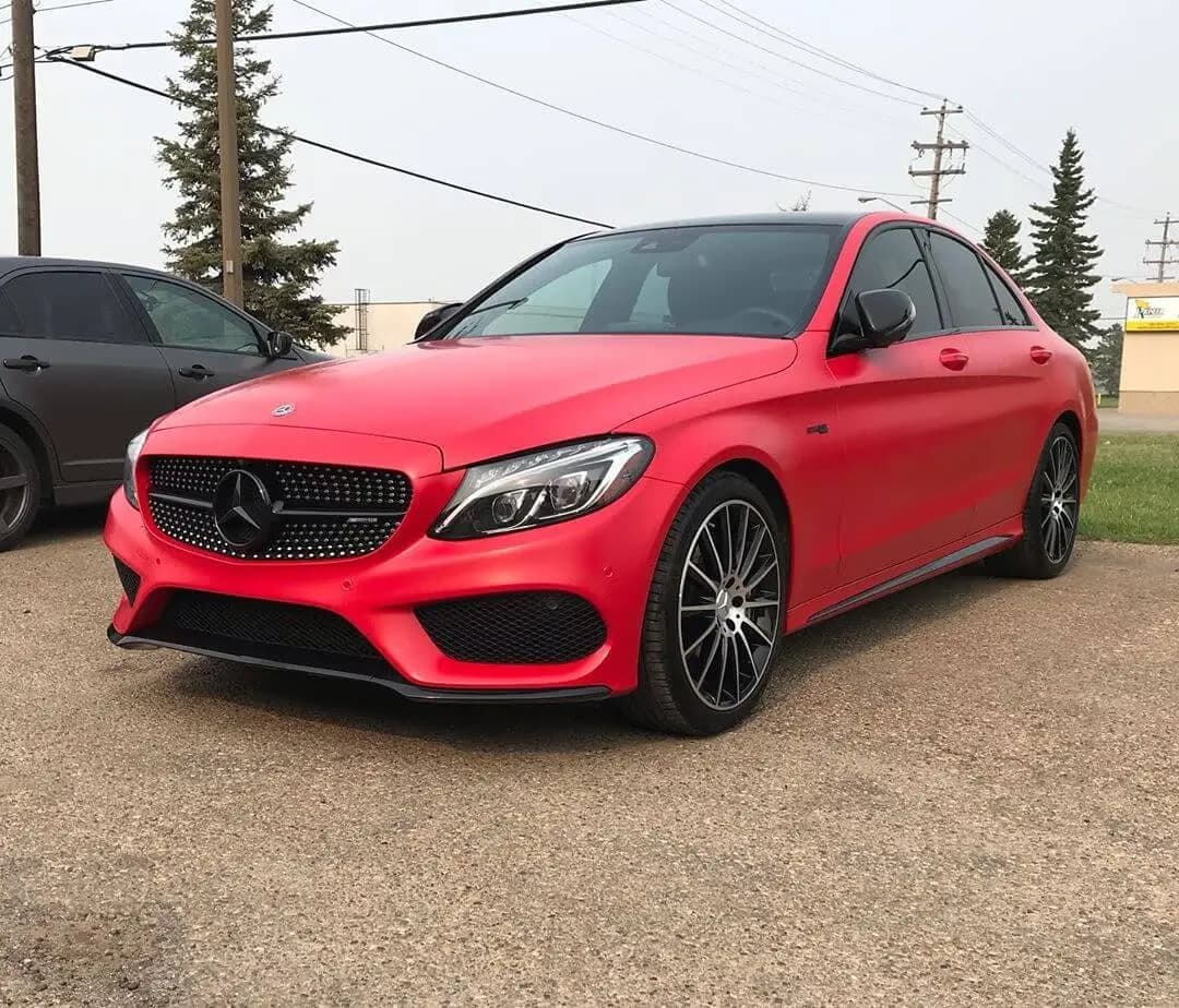 Mercedes-Benz sedan wrapped in Satin Carmine Red, front three-quarter view on a gravel lot