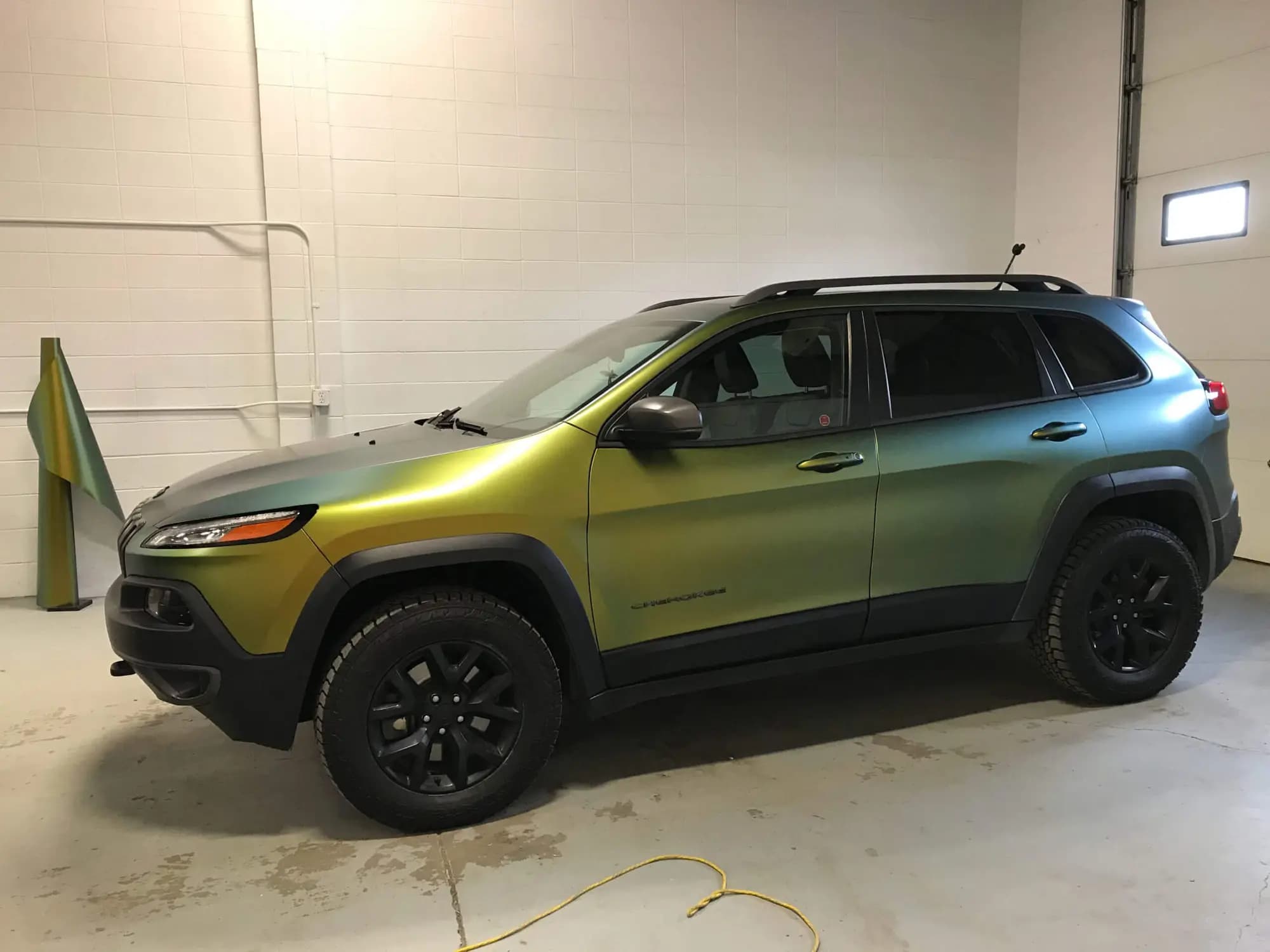 Jeep Cherokee wrapped in ColorFlow Fresh Spring, driver-side profile inside a garage bay, with an offcut of the same film leaning against the wall