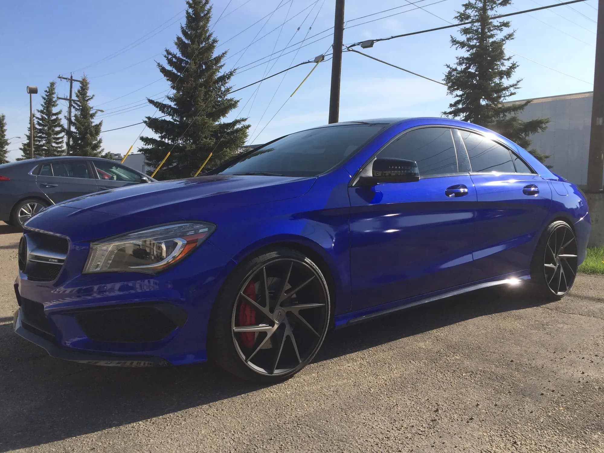 Mercedes-Benz CLA sedan wrapped in Gloss Blue Raspberry, parked outdoors in full sun on dark aftermarket wheels