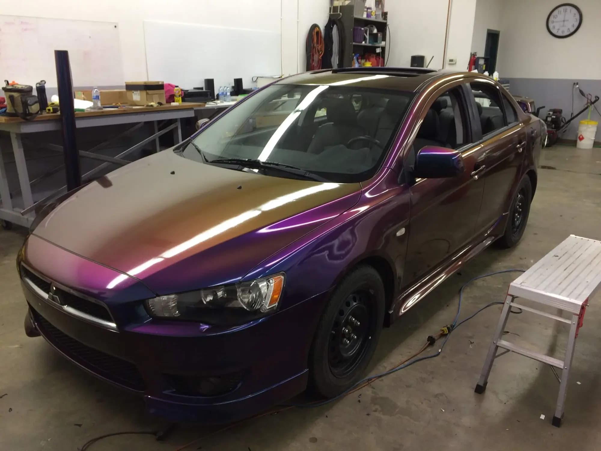 Mitsubishi Lancer sedan wrapped in Gloss Flip Deep Space in our shop, the hood shifting from bronze through magenta to blue-violet