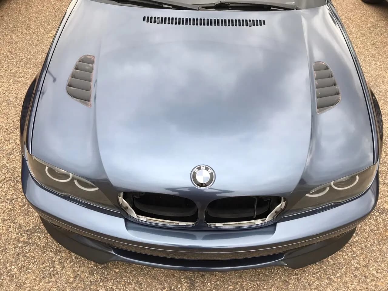 The hood and front end of a BMW wrapped in Gloss Glacier Grey, the glossy panel mirroring cloud overhead