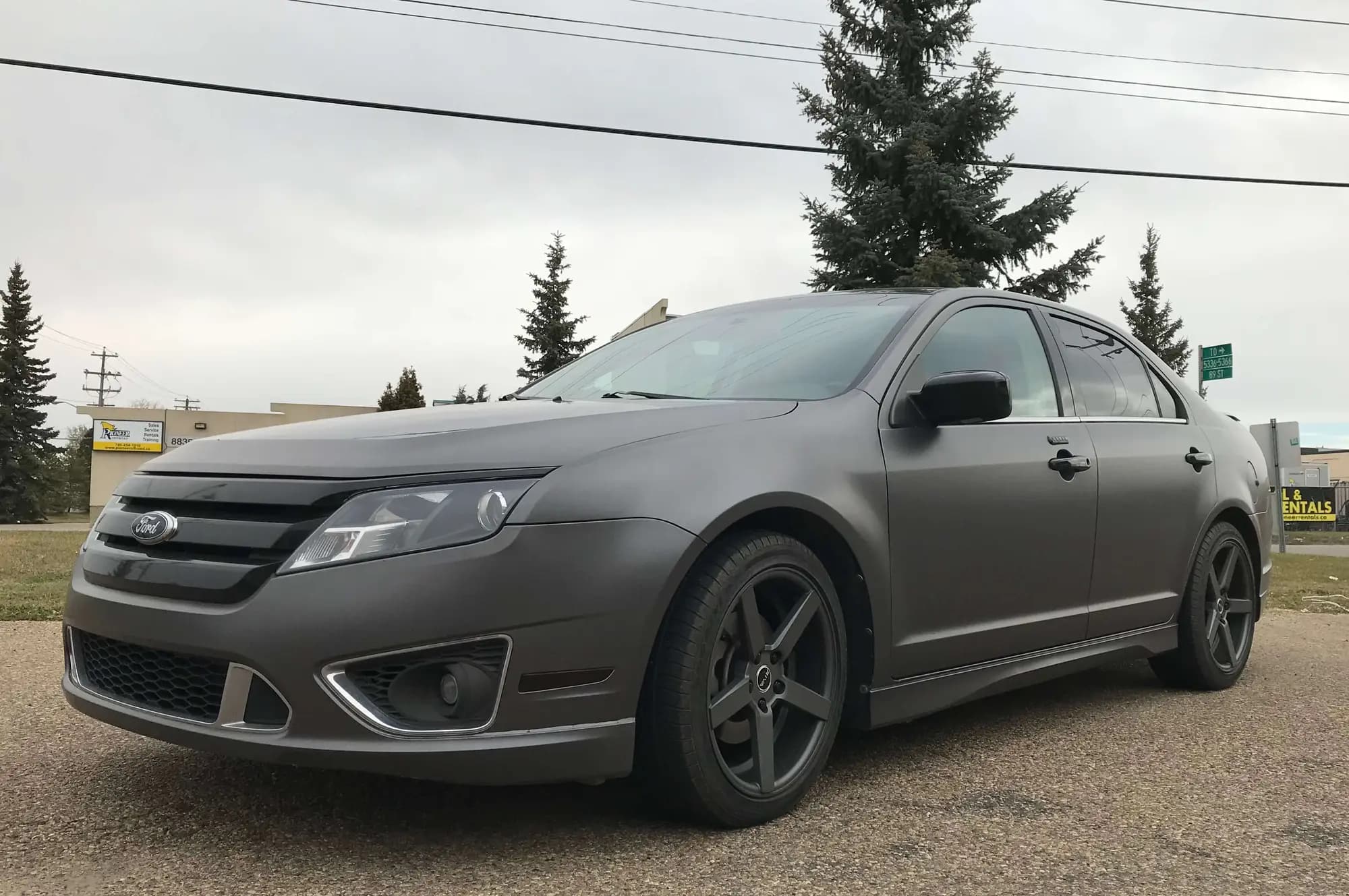 A Ford Fusion sedan wrapped in Satin Dark Gray, front three-quarter view showing the gloss black grille and dark wheels