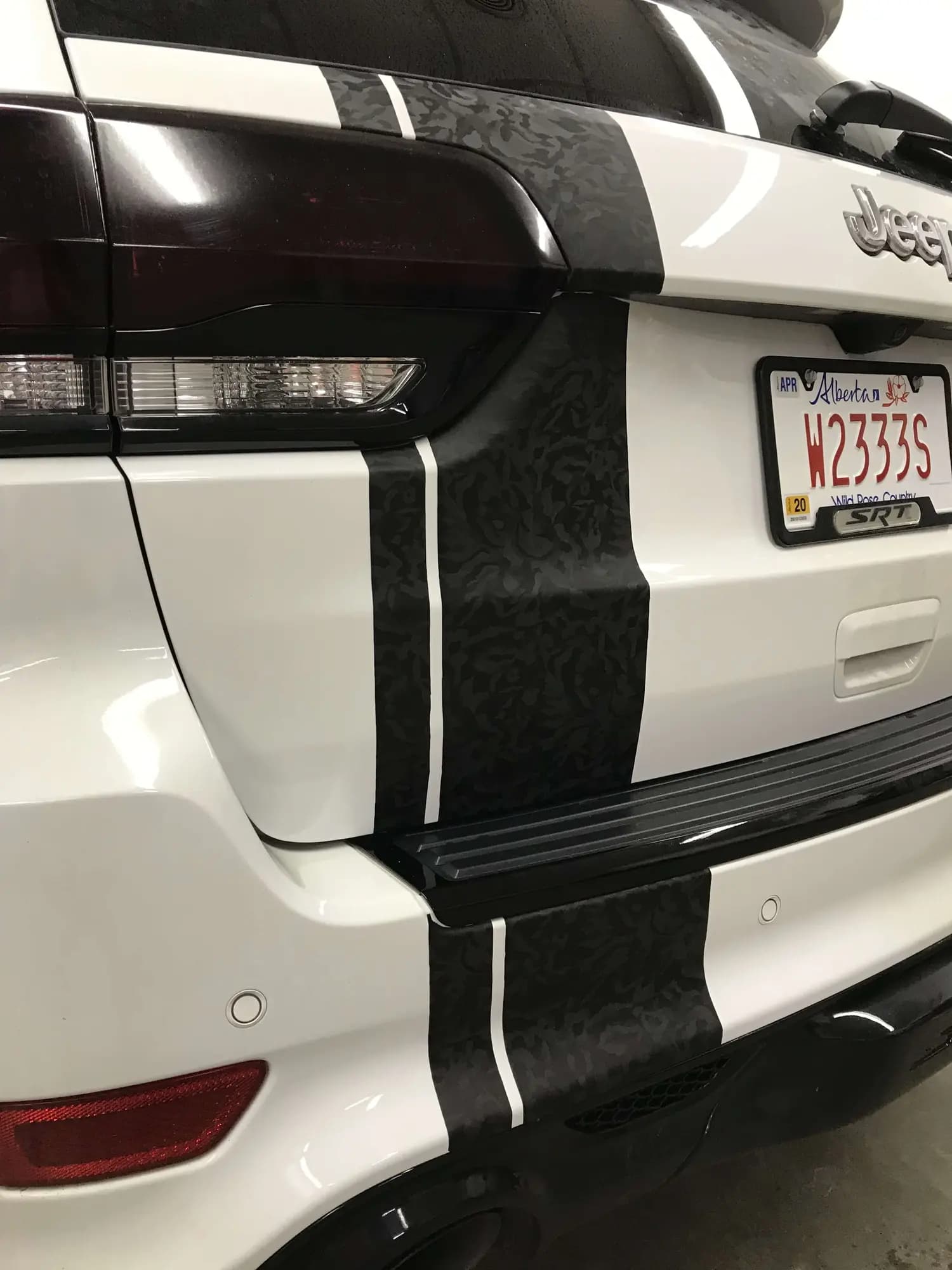 Close-up of the rear of a white Jeep SUV with Shadow Black textured stripes running over the tailgate and bumper